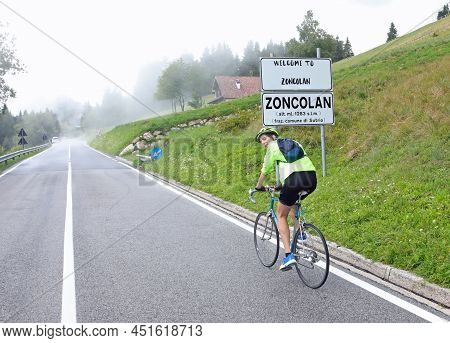 Young Sporty Boy Pedaling With The Cycling Bike And The Sign Indicating The Locality Zoncolan In Nor