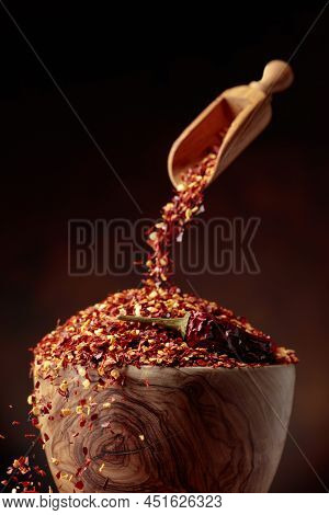 Chilli Flakes Are Poured Into A Wooden Dish. Chilli Flakes And Dried Chili Peppers On A Brown Backgr