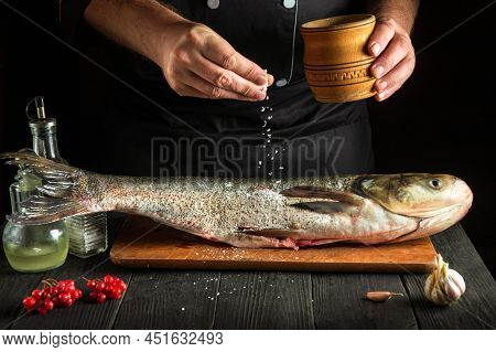 The Chef Prepares Silver Carp Herring In The Kitchen. The Cook Sprinkles Salt On The Fish. Work Envi