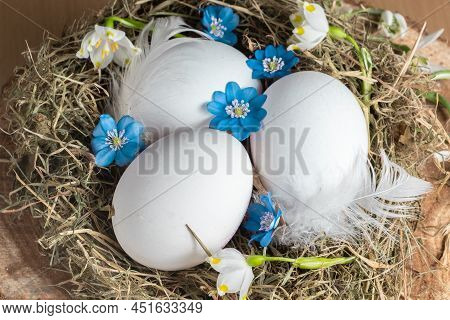 White Chicken Eggs And Blue Flowers In A Hay Nest. Easter Traditional Decor.