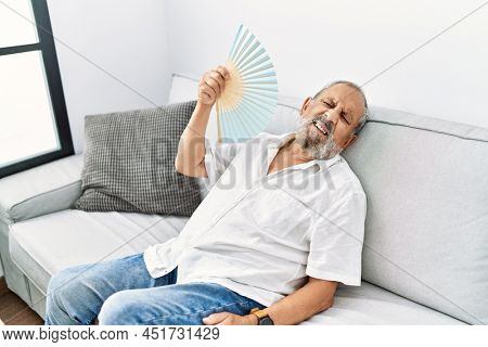 Senior grey-haired man using handfan at home