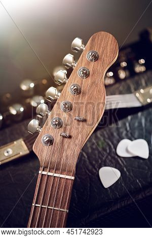 Close Up On The Headstock Of Electric Guitar Against Black Amp And White Picks, Lense Flares