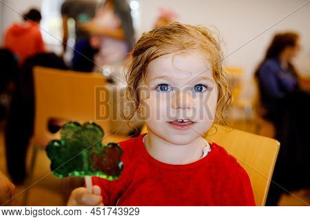 Cute Toddler Girl With Cloverleaf Lollipop In Irish Pub Or Cafe. Child Resting With Parents And Eati