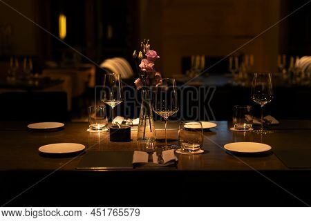 Romantic Evening Table Setting With Wine Glasses And Flowers In Unrecognizeble Restaurant