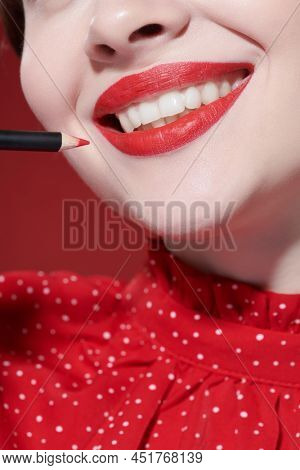 Makeup and cosmetics. Portrait of a beautiful girl model with gorgeous bright red lipstick smiling and applying a red lip liner to overline her lips. Close up shot.