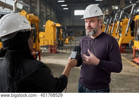 Mature Bearded Engineer In Work Helmet Speaking In Microphone And Giving Interview To Reporter Durin