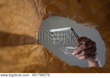 A Hand Takes Out A Shopping Cart In A Paper Bag. A Mature Man's Hand Holds An Empty Shopping Cart Ov