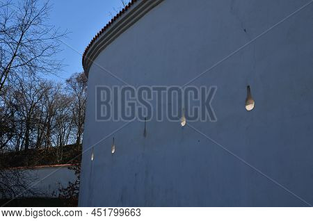 Defensive Wall Of The Castle With Loopholes. Zigzagging White Wall With Roof Tiles Roofing. Under Th
