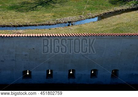 Defensive Wall Of The Castle With Loopholes. Zigzagging White Wall With Roof Tiles Roofing. Under Th