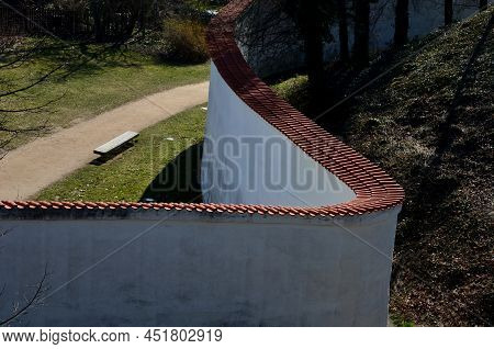 Defensive Wall Of The Castle With Loopholes. Zigzagging White Wall With Roof Tiles Roofing. Under Th