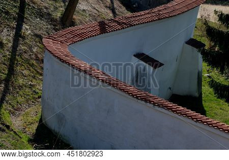 Defensive Wall Of The Castle With Loopholes. Zigzagging White Wall With Roof Tiles Roofing. Under Th