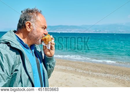 Bearded Mature Man At Spring Seaside Eating Hot Palatable Arancina (deep Fried Rice Balls With Meat)