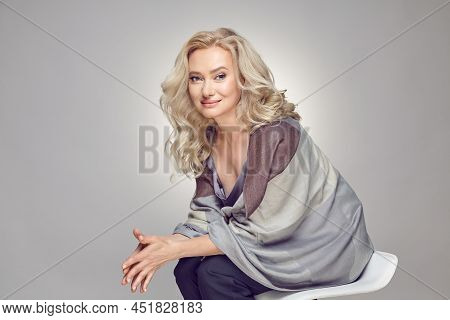 Mature Older Woman Wearing In Tippet Plaid Sitting On Chair Over Grey Isolated.