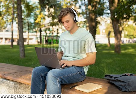 Technology And Studentship Concept. Male Student Using Laptop Computer And Wearing Headphones, Sitti