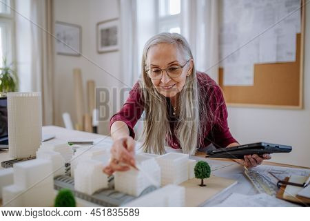 Senior Woman Eco Architect With Model Of Modern Bulidings Working In Office.