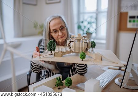 Senior Woman Architect Holding Model Of Modern Eco Buliding In Office