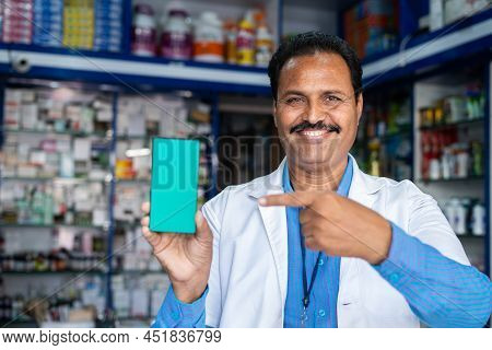 Smiling Medical Store Pharmacist In Uniform Showing Green Screen Mobile Phone By Pointing Finger At 