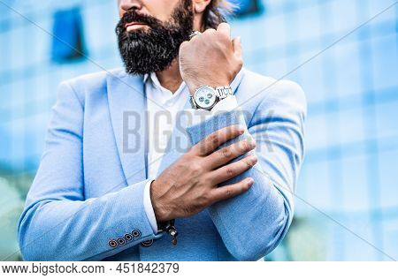 Businessman Points To His Watch On The Background Of The Town. Man Holds His Watch. Portrait Success