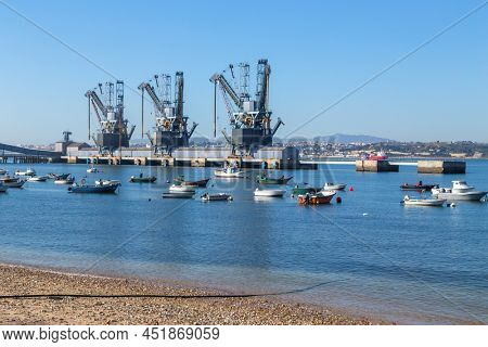 Trafaria; Portugal - March 01; 2022: Deep water terminal and silo for grain, derived products and oleaginous products in Trafaria, Portugal with fishing boats near the beach