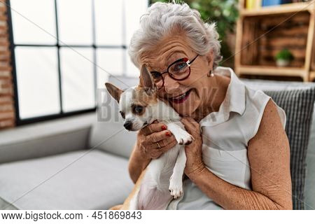 Senior grey-haired woman smiling confident holding chiuahua sitting on sofa at home