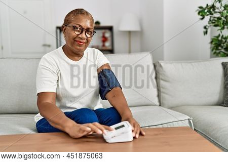 Senior african american woman smiling confident using tensiometer at home