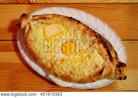 Plate Of Adjaruli Khachapuri, Traditional Georgian Cheese And Egg Bread Served On Wooden Table