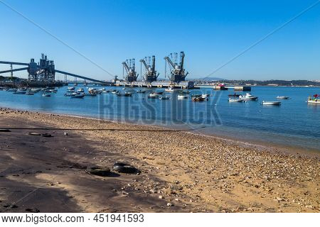 Trafaria; Portugal - March 01; 2022: Deep water terminal and silo for grain, derived products and oleaginous products in Trafaria, Portugal with fishing boats near the beach