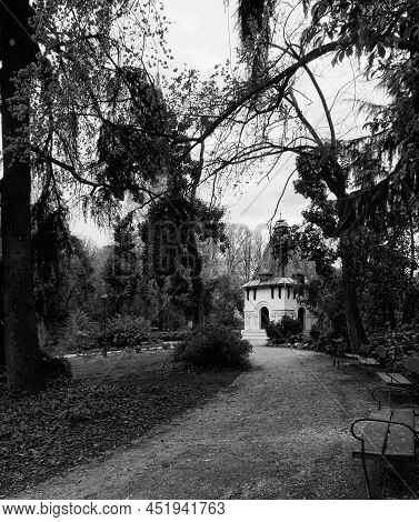 Landscape Of A Park In Black And White With A Path. A Row Of Benches And A Booth In The Background. 