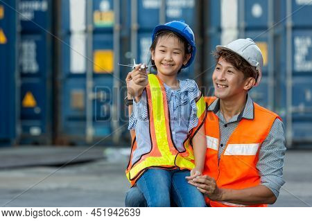 Father And Little Daughter Wearing A Safety Helmet At Container Cargo Site. Business Heir Concept. H