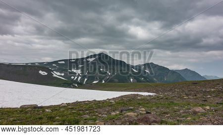 In A High-altitude Valley There Is Melted Snow. There Is Scant Vegetation On The Rocky Soil. A Pictu
