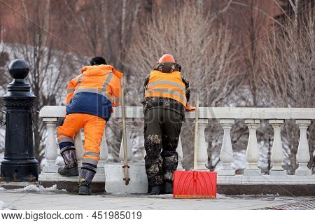 Two Janitors With Shovels Standing On Park Trees  Background. Labour Migrants During Rest, Street Cl