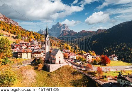Aerial drone flight over San Lorenzo Catholic church in Selva di Cadore village. Biautiful small city in autumn Dolomites mountains. Dolomite Alps, Province of Belluno, Italy