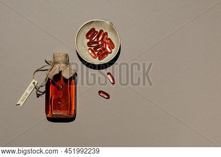 Transparent Container With Algae Oil And Jelatin Oil Capsules In Clay Saucer. Glass Bottle Is Tied W