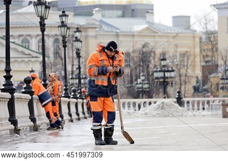 Moscow, Russia - March 2022: Worker With Shovel Standing With Smartphone On Manezh Square. Street Cl