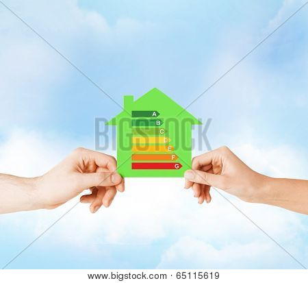 energy saving, real estate and family home concept - closeup of couple hands holding green paper house with energy efficiency rating