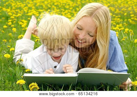 Happy Mother And Child Reading Book Outside In Meadow
