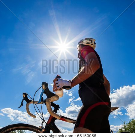 Cyclist resting and drinking isotonic drink. Backlight, sunny summer day.