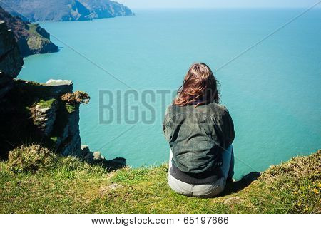 Young Woman Sitting On Edge Of Cliff