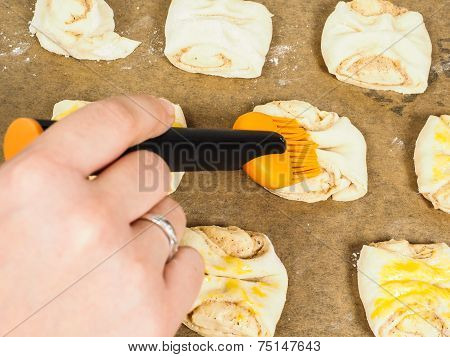 Person Glazing Plaited Baked Goods With Egg Wash