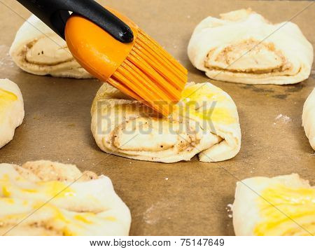 Closeup Of Person Glazing Plaited Baked Goods With Egg Wash
