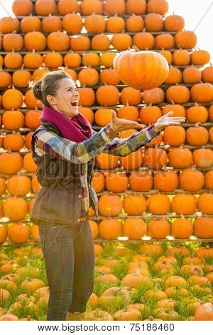 Happy Young Woman Throwing Pumpkin In Front Of Pumpkin Rows