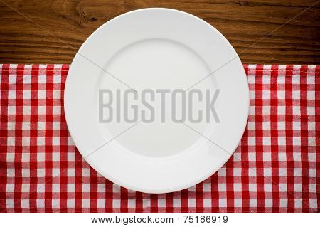 Empty plate with fork and knife on tablecloth over wooden