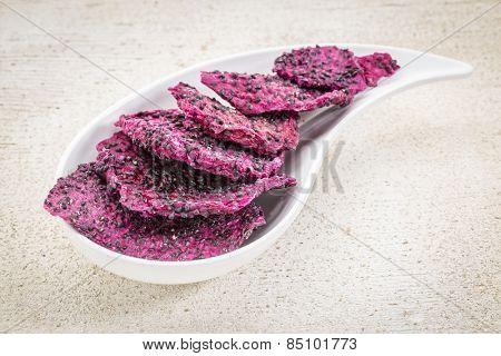 slices of dried red dragon fruit on a teardrop shaped bowl against rustic wood