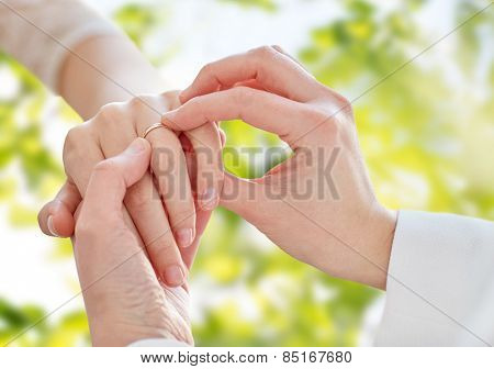 people, homosexuality, same-sex marriage, summer and love concept - close up of happy lesbian couple hands putting on wedding ring over green tree leavers background