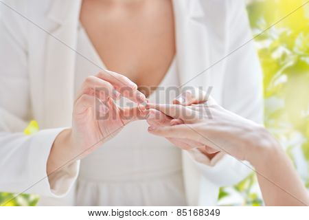 people, homosexuality, same-sex marriage, summer and love concept - close up of happy lesbian couple hands putting on wedding ring over green tree leavers background