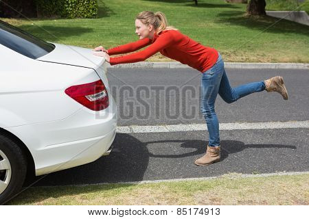 Young woman pushing her broken down car in the street