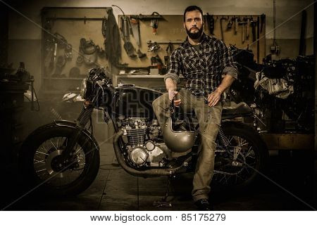 Rider and his vintage style cafe-racer motorcycle in customs garage 