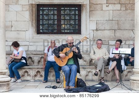 DUBROVNIK, CROATIA - MAY 26, 2014: Street guitar player  performing on Stradun.  Stradun is 300 meters long main pedestrian street in Dubrovnik.