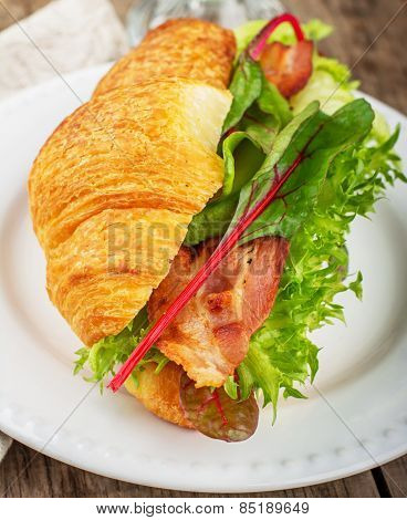 Fresh croissant for breakfast stuffed with bacon, lettuce, chard, and avocado on a light background