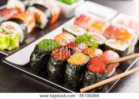Delicious sushi rolls served on black plate and stone